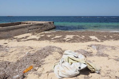 ﻿﻿A côté du site archéologique de Sabratha le 20 juillet, un Zodiac blanc est enfoui dans le sable, avec un tas d'habits, des déchets et des bidons d'eau. Crédits : SAMUEL GRATACAP POUR LE MONDE