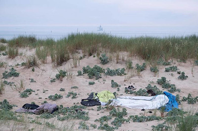 Des effets personnels abandonnés par des migrants dans les dunes de Sangatte. Au loin, un ferry pour l’Angleterre, Calais, juin 2021. © Olivier Favier.