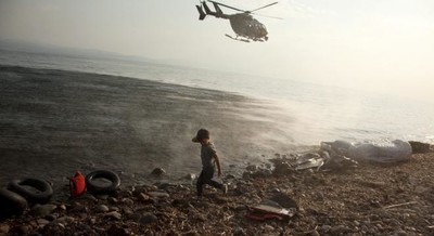 Août 2015 : un hélicoptère de l’agence Frontex décolle au-dessus d’un enfant syrien qu’il vient de déposer sur l’île grecque de Lesbos. © Antonis Pasvantis / Reuters